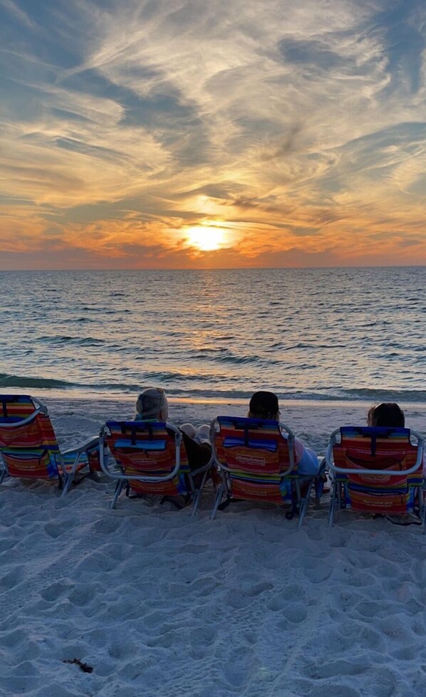 Un coucher de soleil sur l’océan, avec des chaises de plage tournées vers la mer.