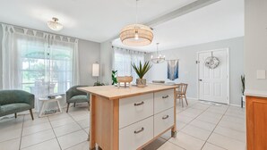 Una cocina moderna con una isla central, suelo de baldosas blancas y una zona de comedor con una silla y mesa.