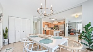 A modern kitchen with wooden cabinets, a central island, and a dining area with a white table and chairs.