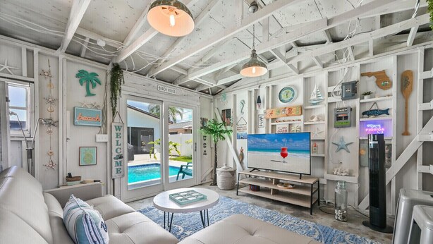 A beach-themed living room with a sofa, TV, and a view of the pool.