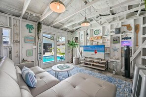 Un salon décoré sur le thème de la plage, avec un canapé, un téléviseur et une vue sur la piscine.