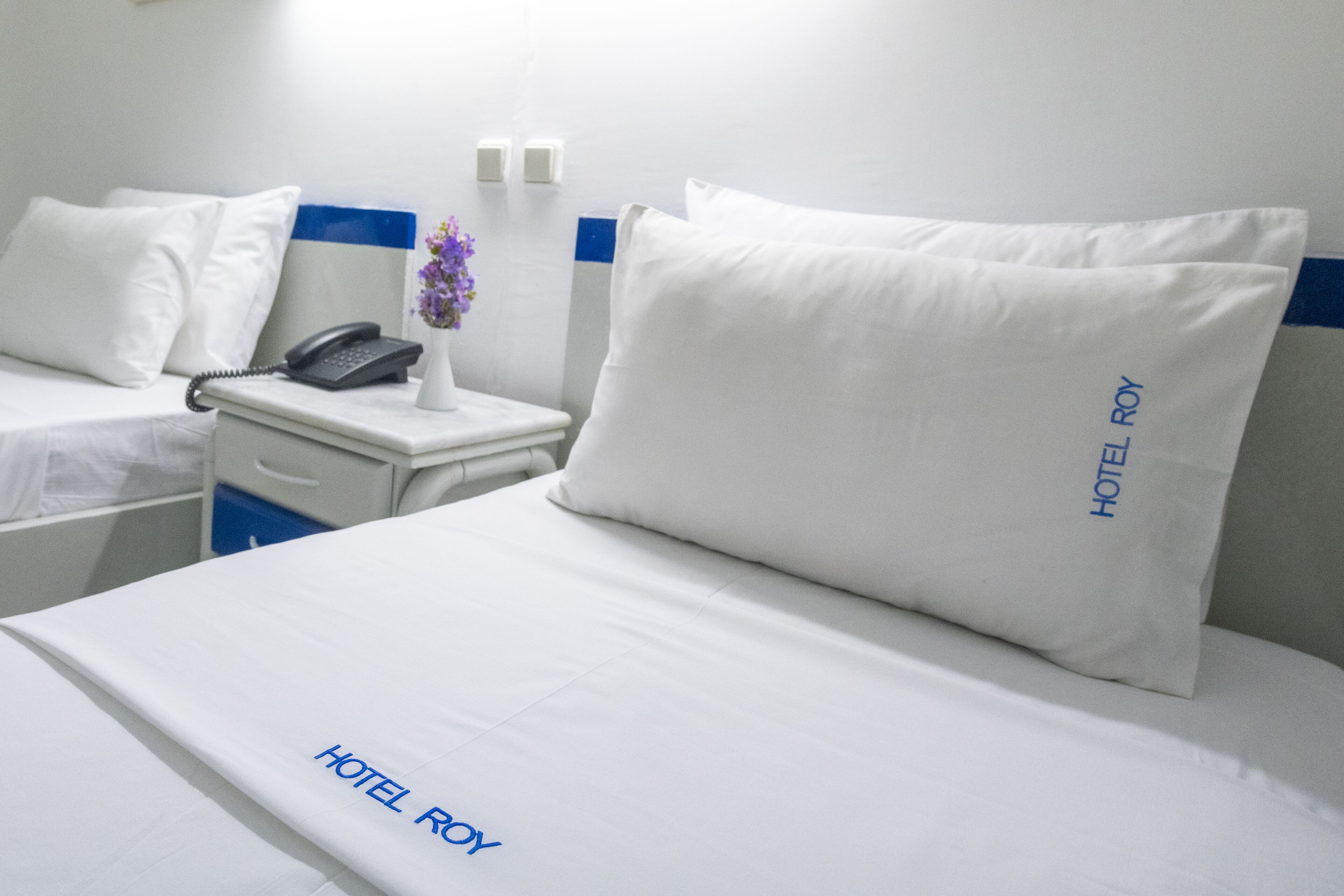 A hotel room with a neatly made bed, a bedside phone, and a nightstand with a vase of flowers.