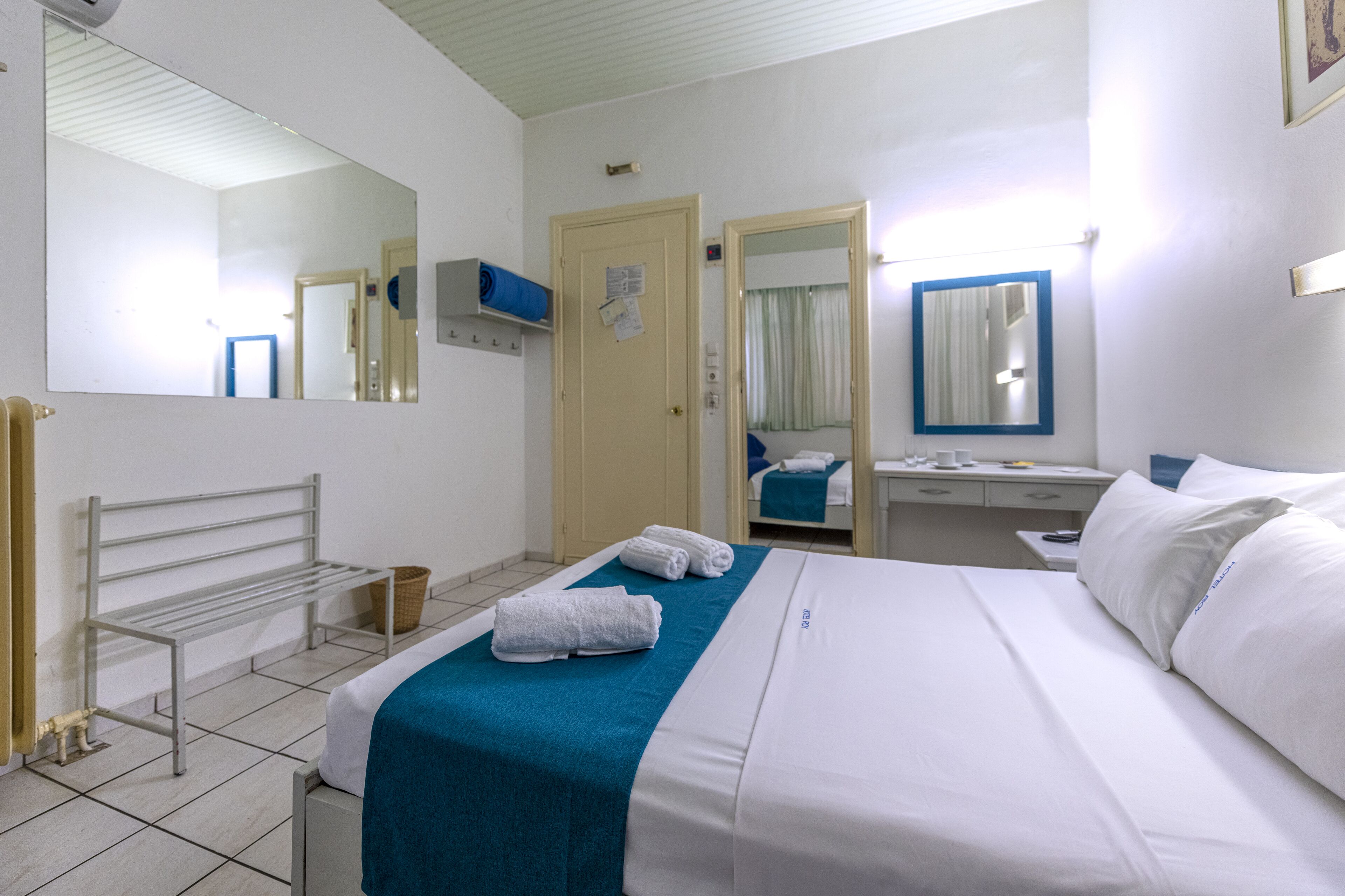A hotel room with a bed, a bench, a desk, and a mirror.