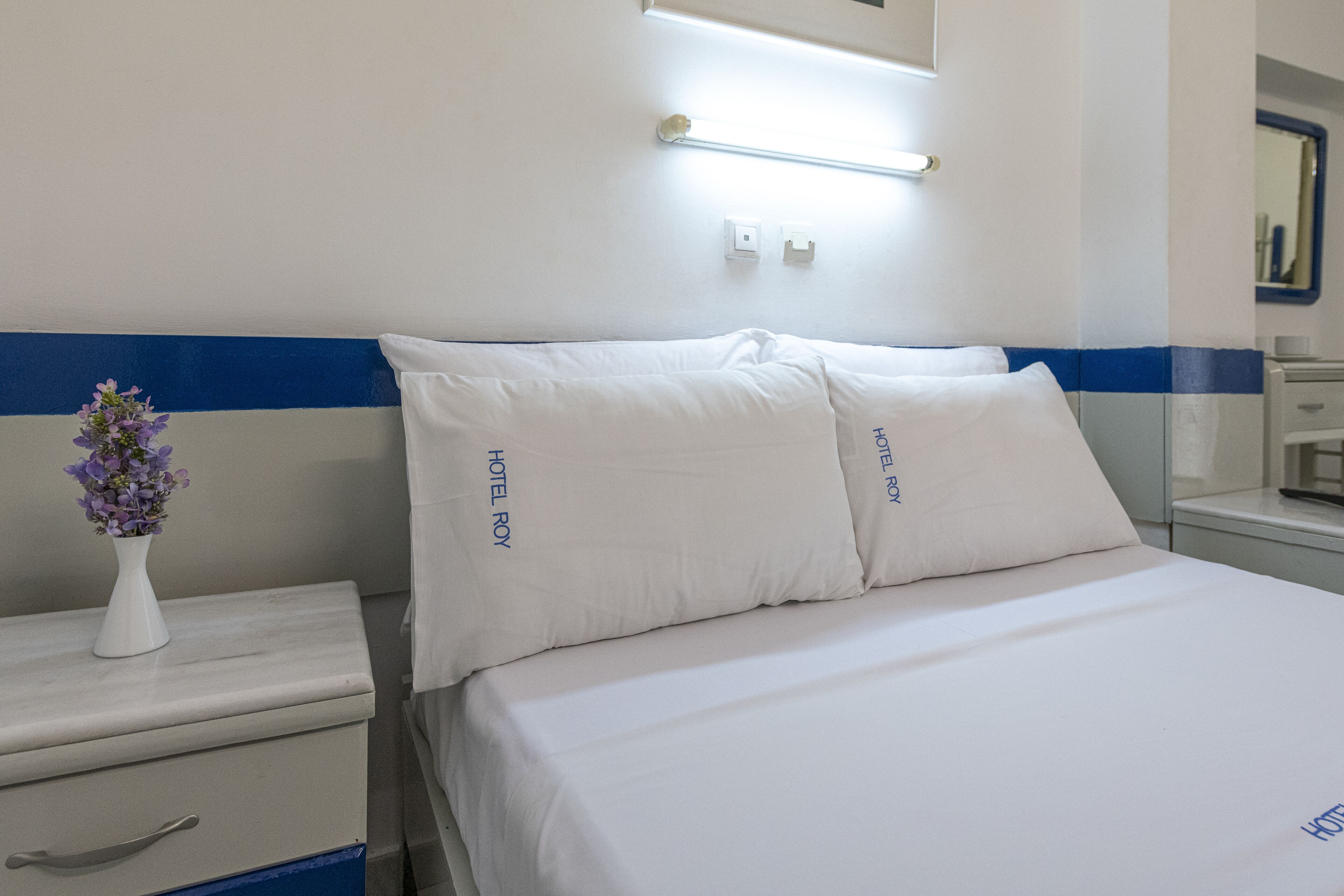 Una habitación de hotel con una cama, una mesita de noche, un florero con flores y un espejo en la pared.