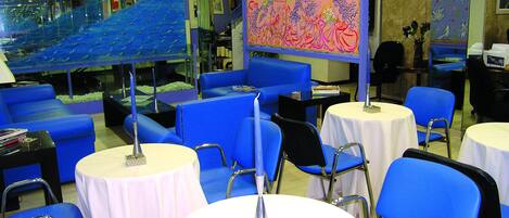 Eine Hotelhalle mit blauen Sitzgelegenheiten, weißen Tischen und einem großen, farbenfrohen Wandgemälde.
