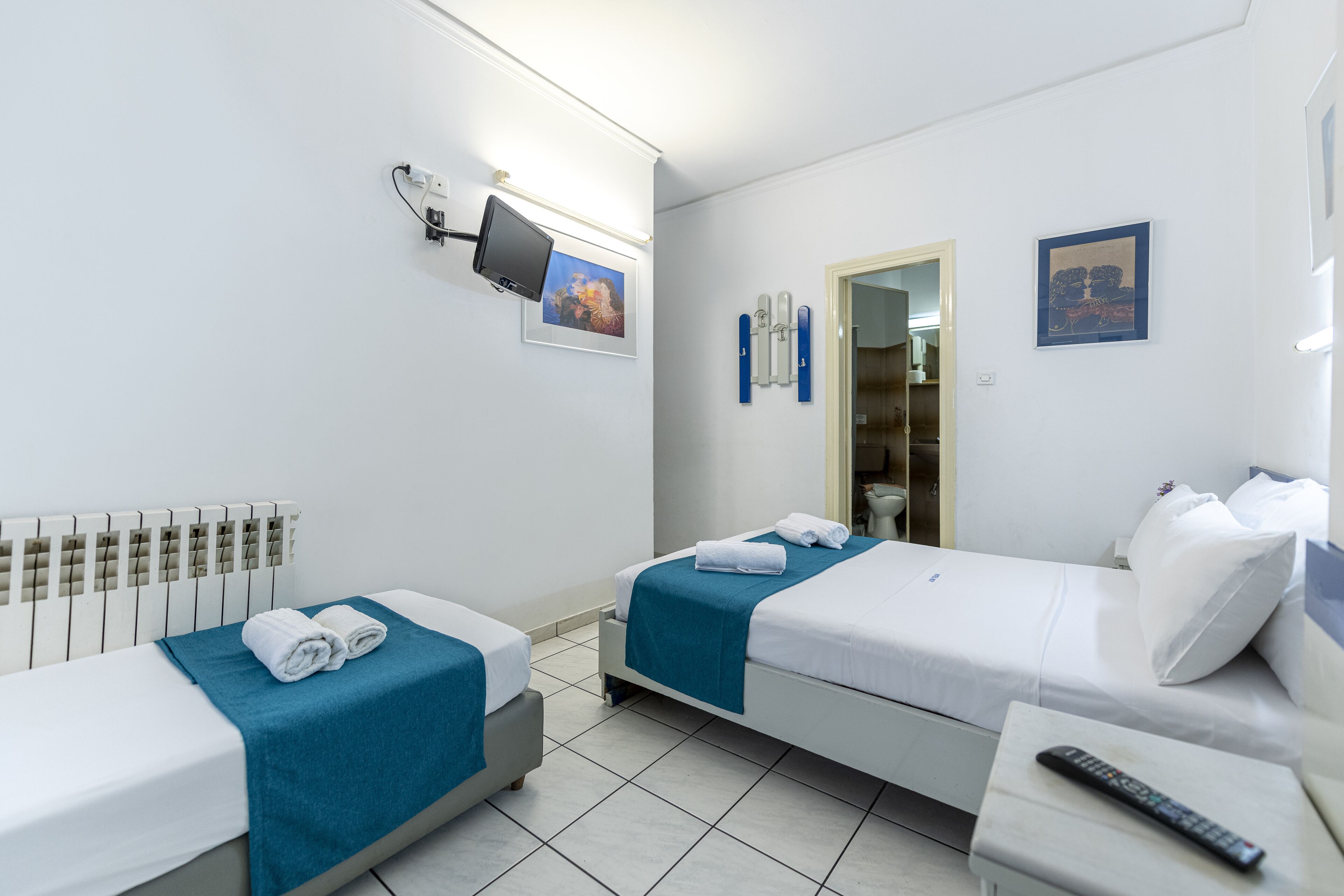 Habitación de hotel con dos camas, un televisor, un espejo y un control remoto sobre una mesita de noche.