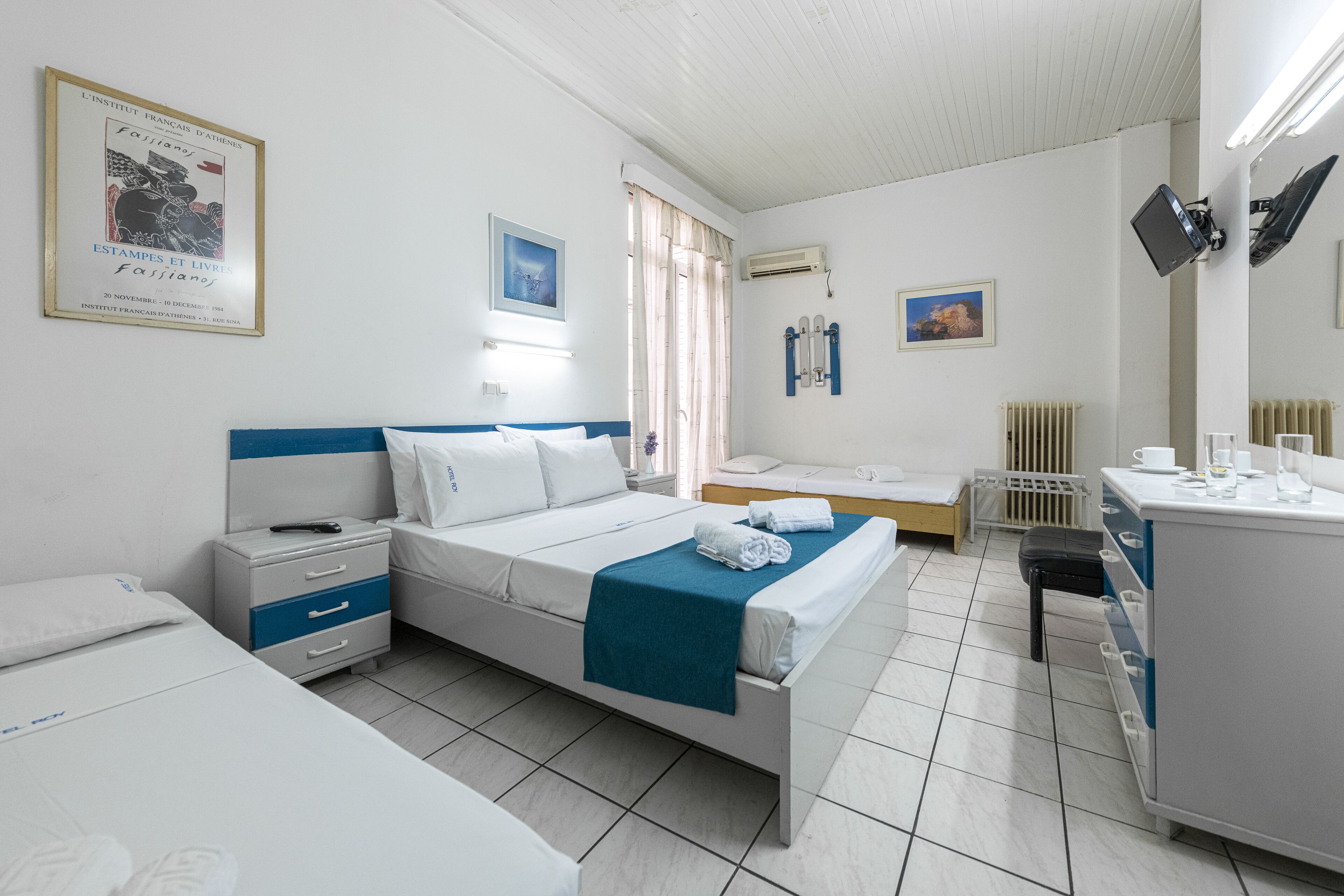 A hotel room with a bed, a desk, a chair, and a radiator.