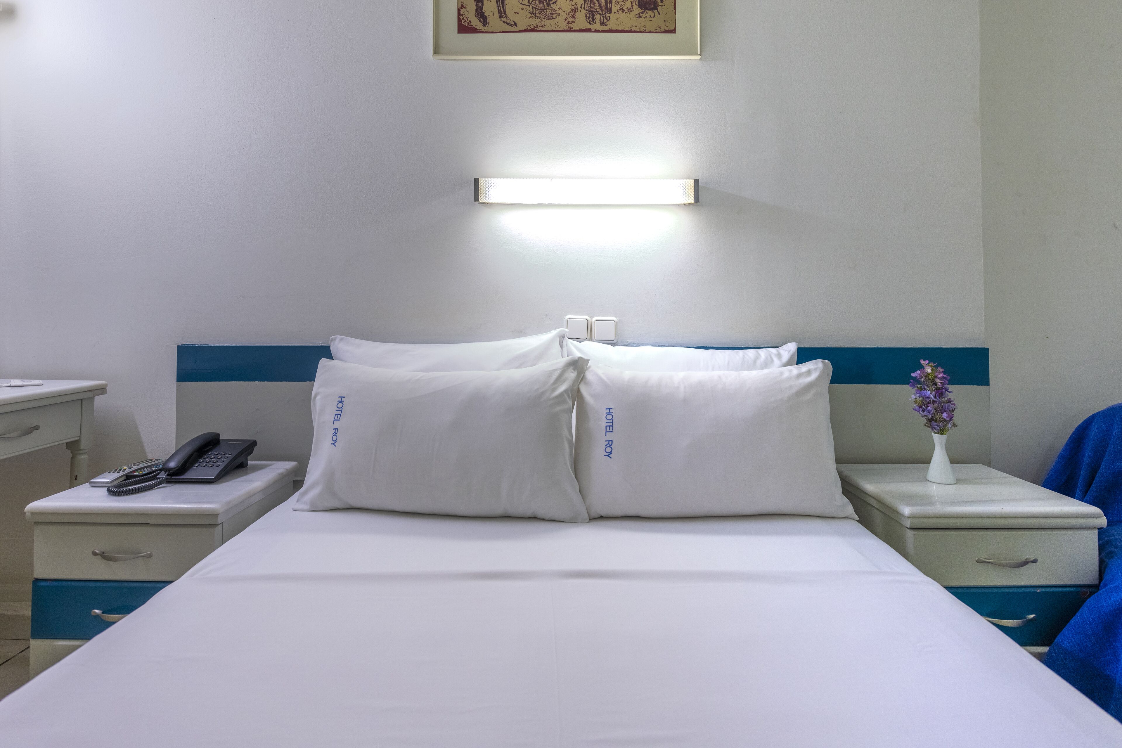 A hotel room with a bed, bedside tables, a phone, and a vase with flowers.