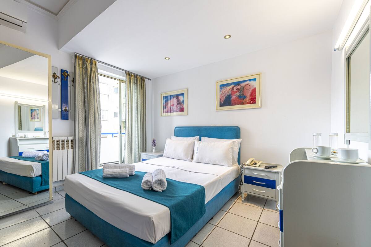A hotel room with a bed, a desk, a chair, a mirror, and two paintings on the wall.
