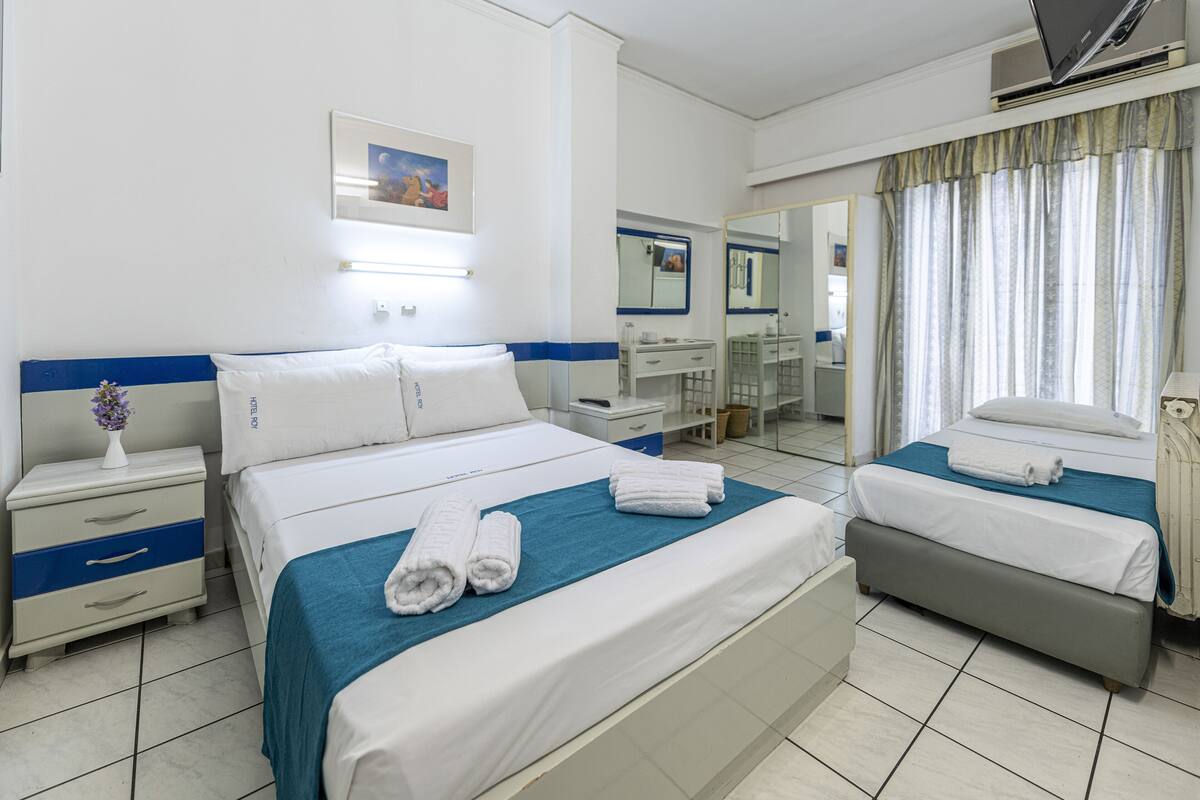 A hotel room with a large bed, a smaller bed, a nightstand, a dresser, a mirror, and a window with curtains.