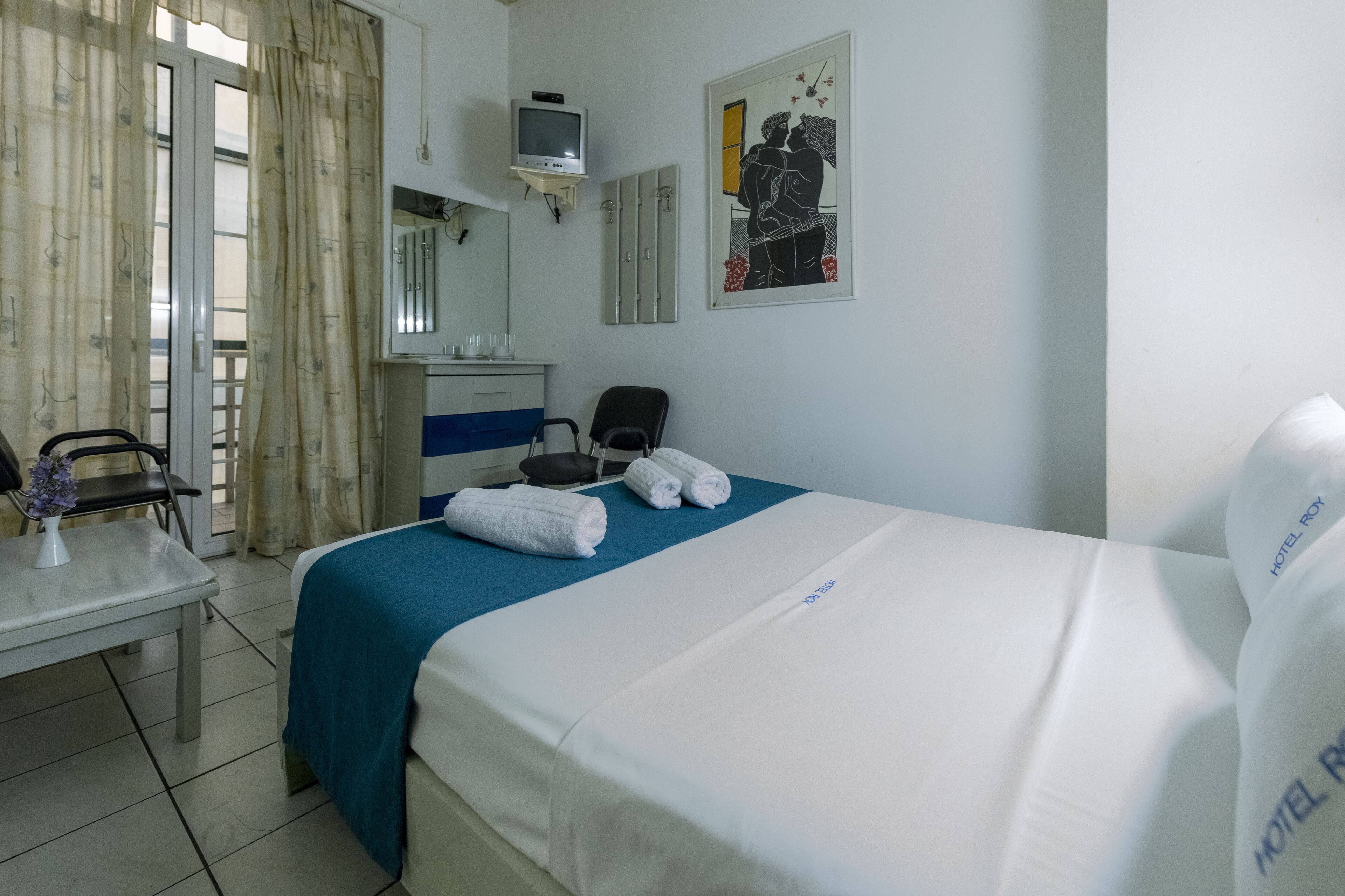 A hotel room with a bed, a desk, a chair, a television, and a painting on the wall.
