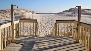 Ein hölzerner Steg führt zu einem Sandstrand bei blauem Himmel.