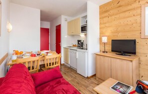 A compact living space with a kitchenette, a dining area with a table and chairs, a television on a wooden cabinet, and a red couch. - 50m from shops, tv, ski locker, 24-28m², Valmeinier (Valmeinier)