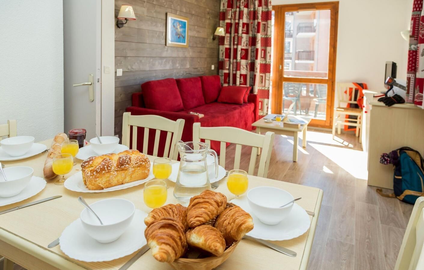 A breakfast setup with croissants and orange juice on a table, a red sofa in the background, and a view of the city through a window.