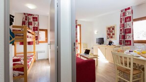 Une chambre avec des lits superposés, un bureau avec un ordinateur portable, une télévision et un coin repas avec des chaises et une table.