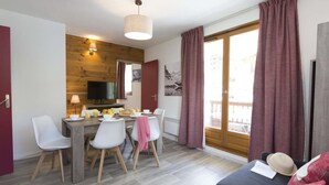 A cozy living room with a sofa, dining area with chairs and a table, a television, and a wooden wall. - 50m from ski slopes, swimming pool, terrace, balcony, tv, ski locker, 30m², Saint Sorlin d'Arves (Saint-Sorlin-d'Arves)