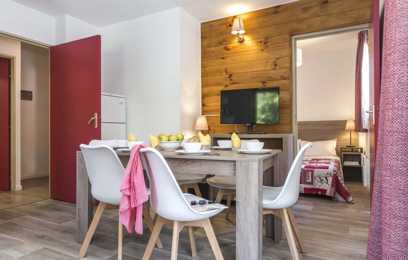 A modern dining area with a wooden wall, a flat-screen TV, and a cozy bed with a patterned blanket.