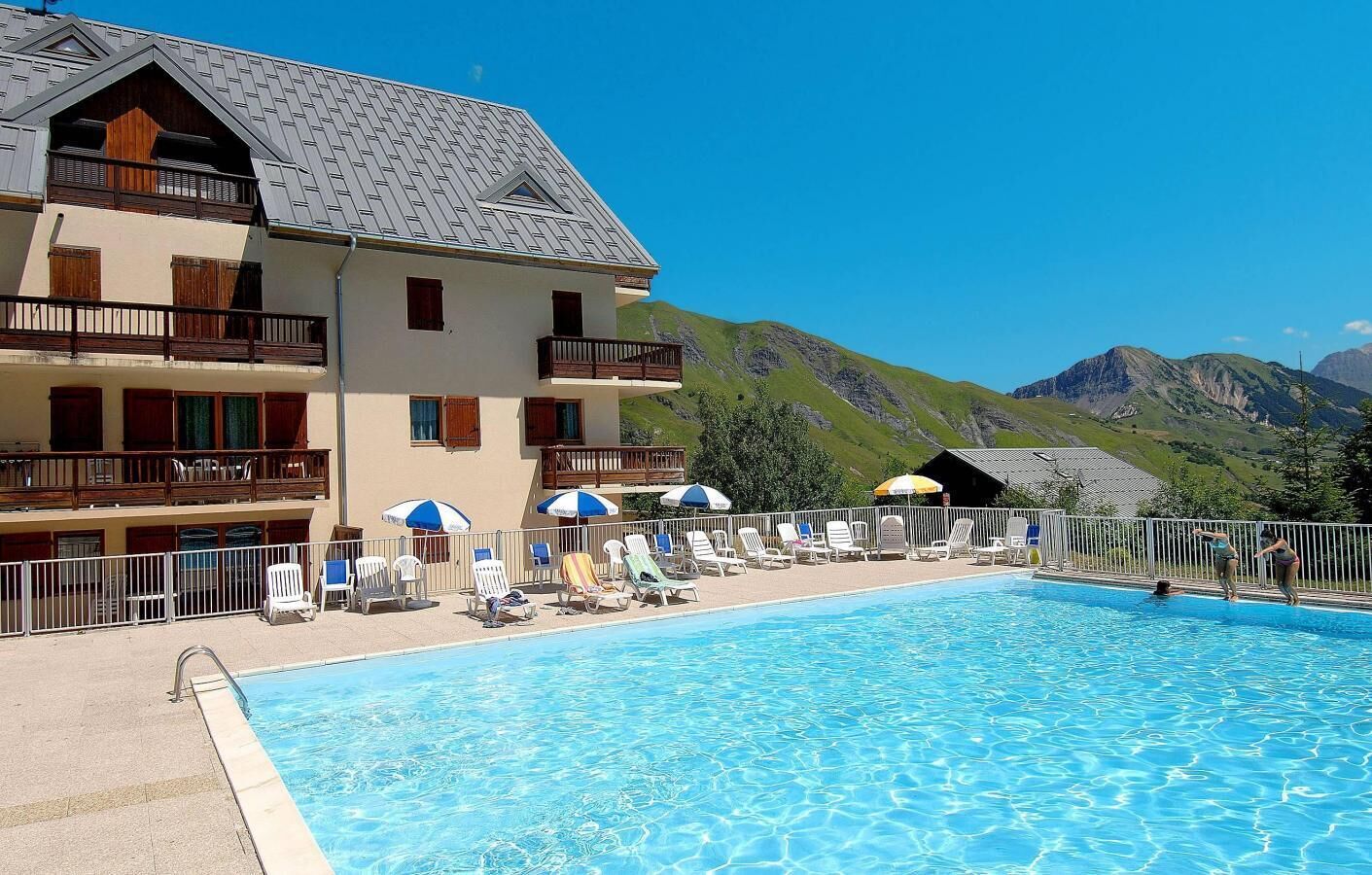 A hotel with a swimming pool, lounge chairs, and umbrellas.