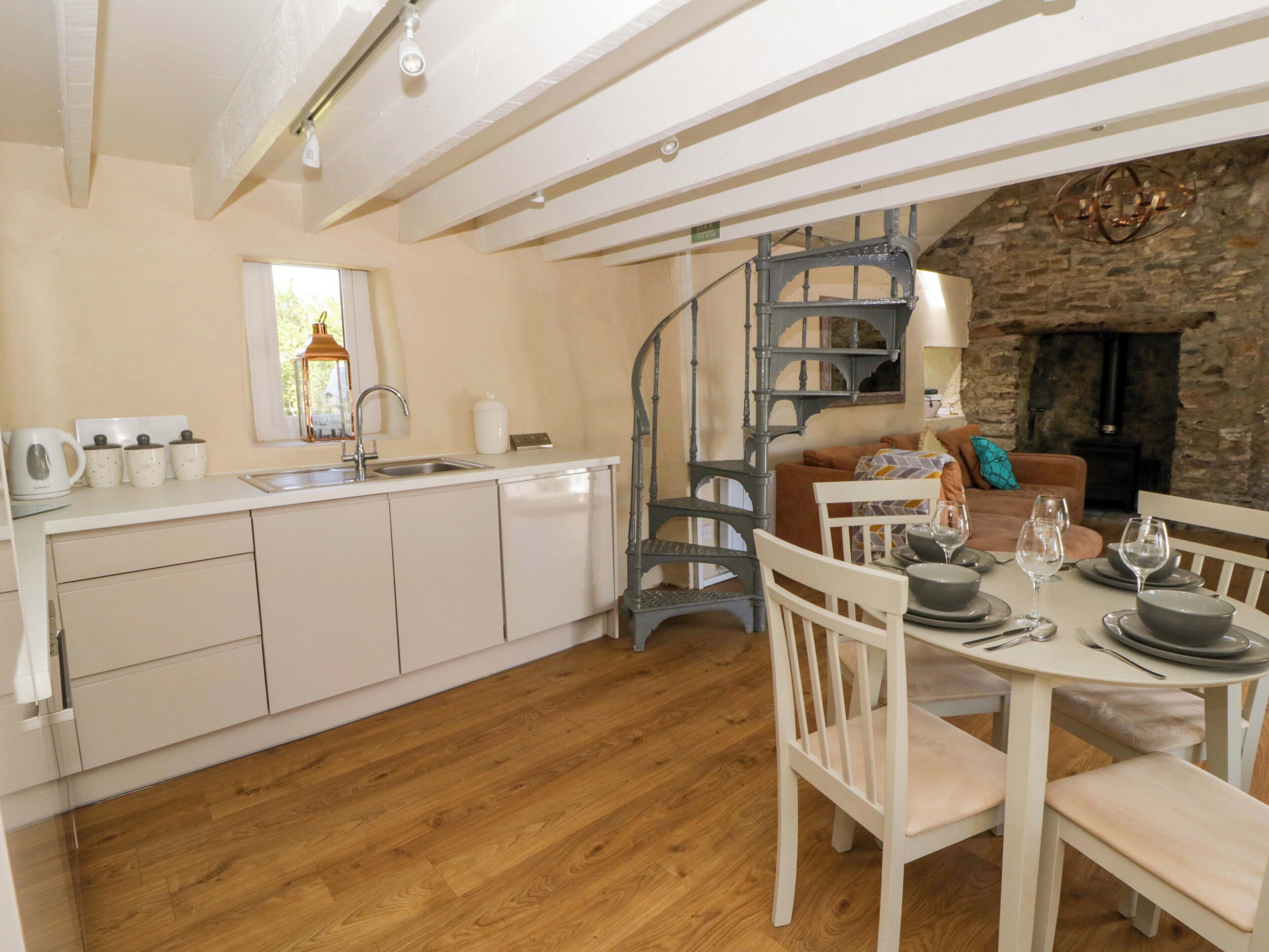 A kitchen with a wooden floor, white cabinets, a sink, and a dining area with a table set for two.