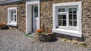 A stone building with a door, two windows, and a gravel driveway. - Cobwebs (Kilgetty)