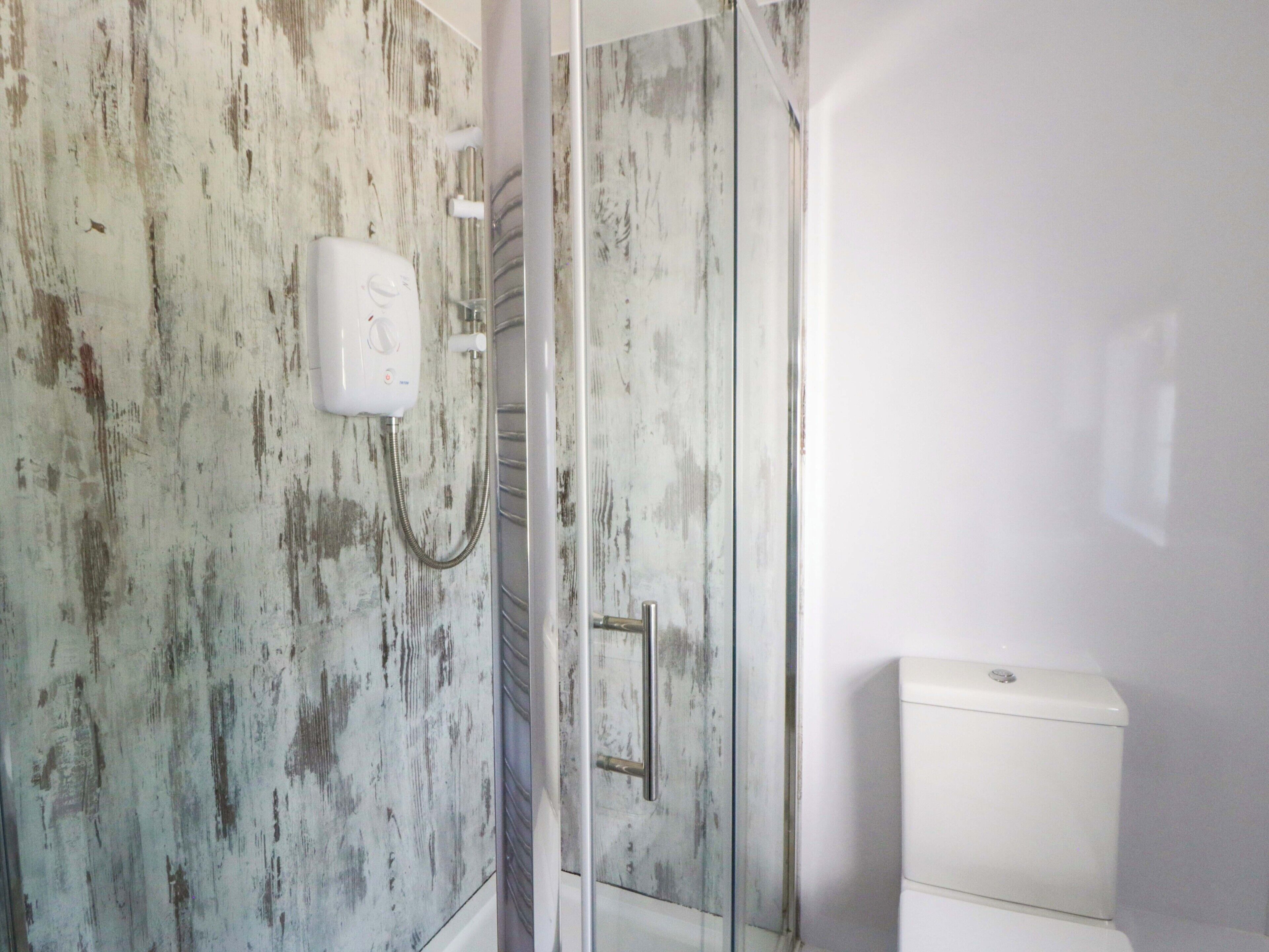 Un baño con diseño de pared rústica, cabina de ducha de vidrio y un inodoro blanco.