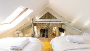 A bedroom with two beds, a skylight, a stone wall, and a wooden floor. - Cobwebs (Kilgetty)