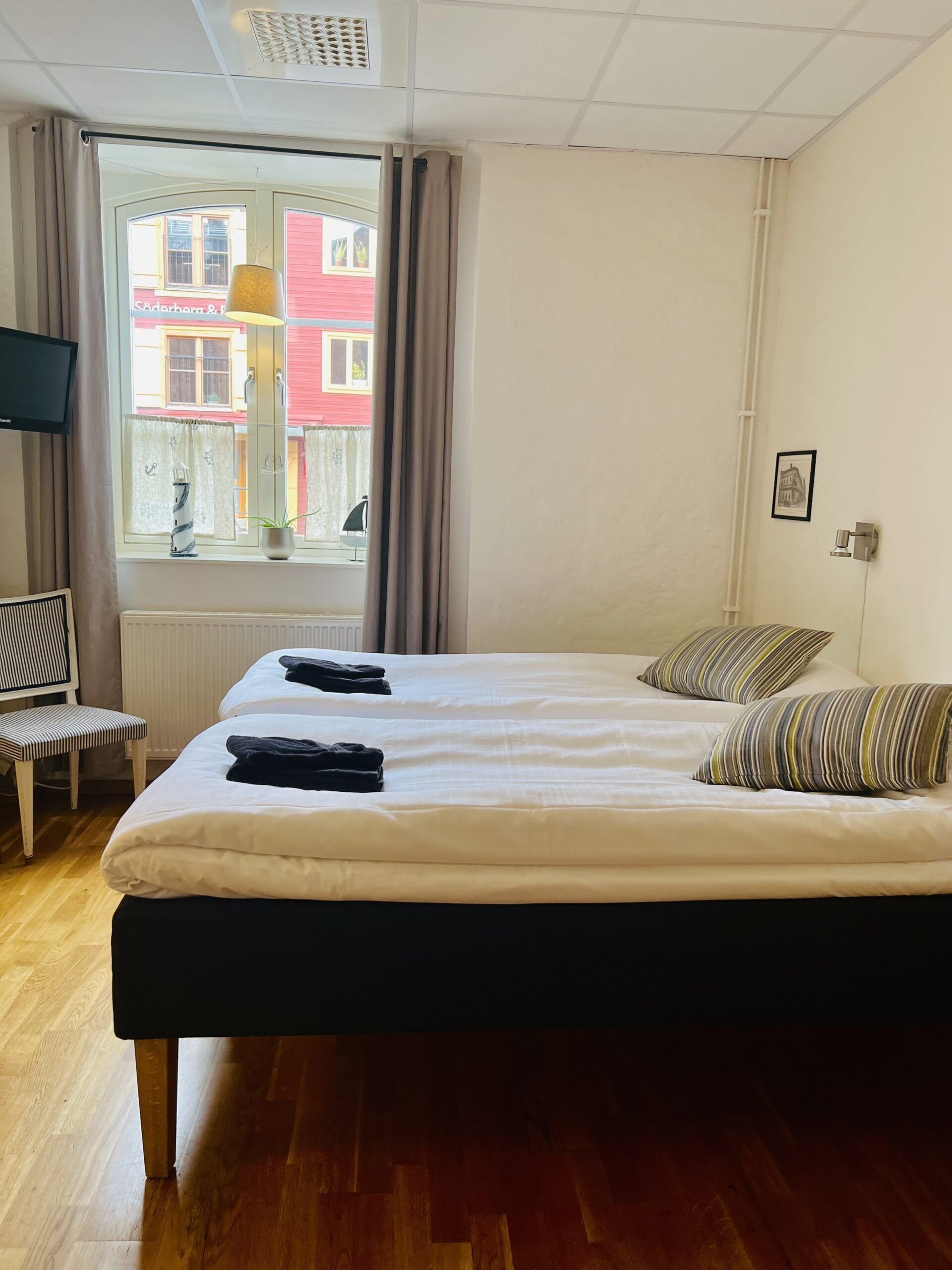 A hotel room with a bed, a chair, a TV, a window with curtains, and a radiator.