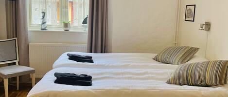 A hotel room with a bed, a chair, a TV, a window with curtains, and a radiator.