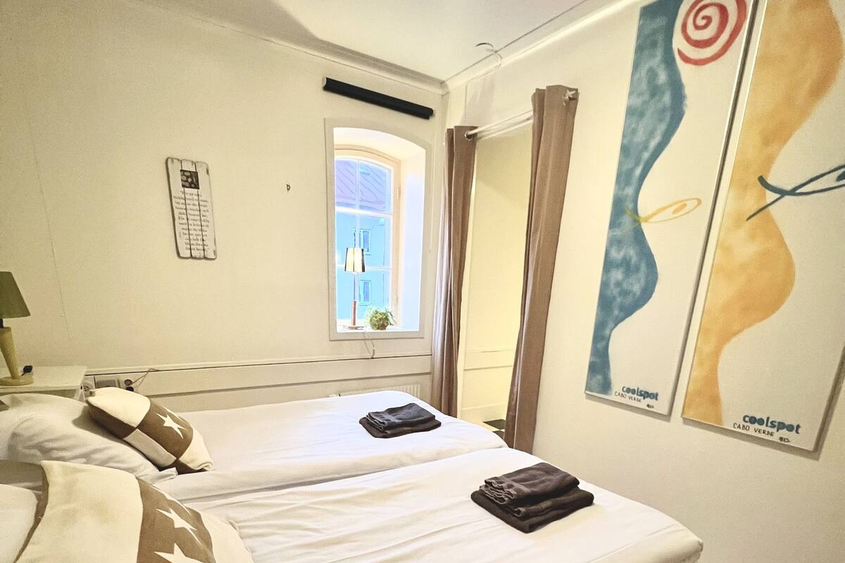 A hotel room with two beds, a window with curtains, a wall-mounted phone, and a poster.