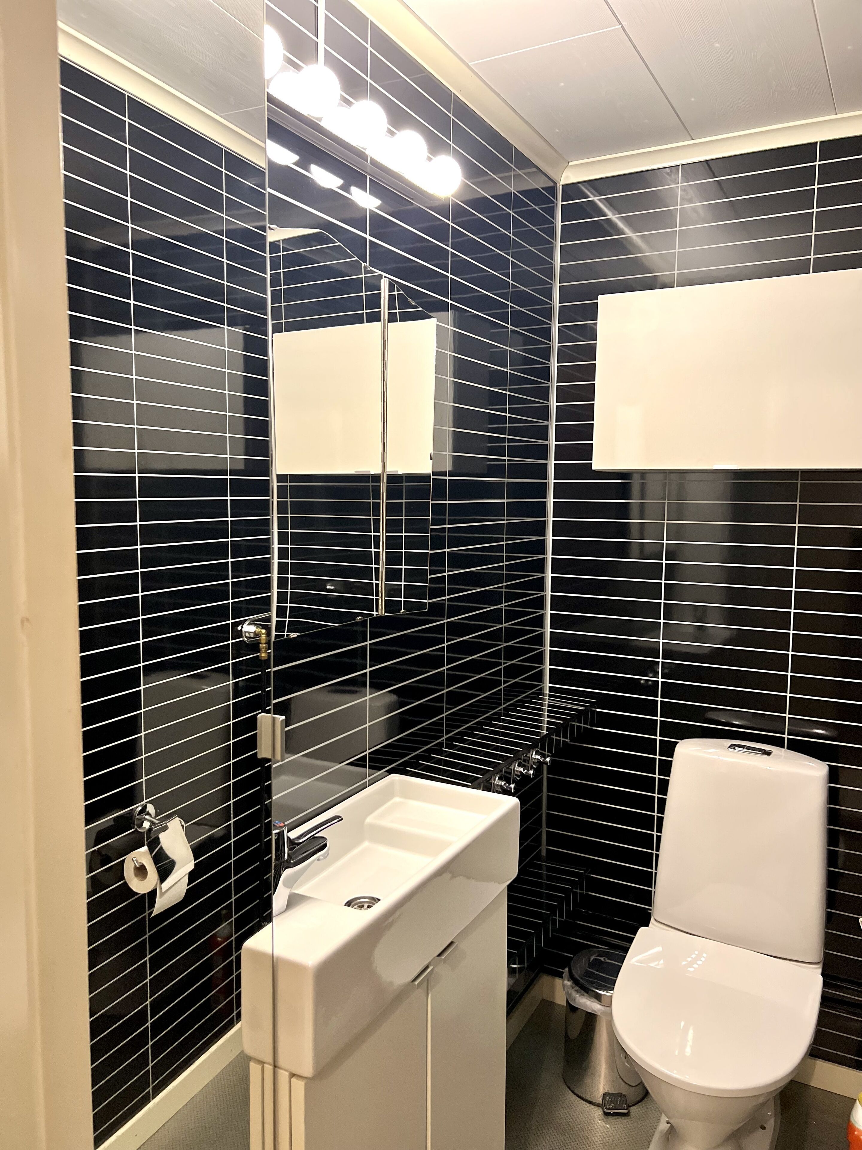 A modern bathroom with black tiled walls, a white sink, and a toilet.