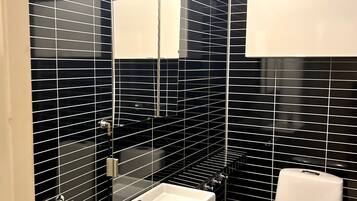 A modern bathroom with black tiled walls, a white sink, and a toilet.