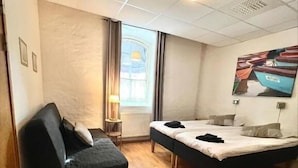 A hotel room with a bed, a small sofa, a window with curtains, a lamp, and a painting on the wall. - Hotell Alderholmen (Gävle)