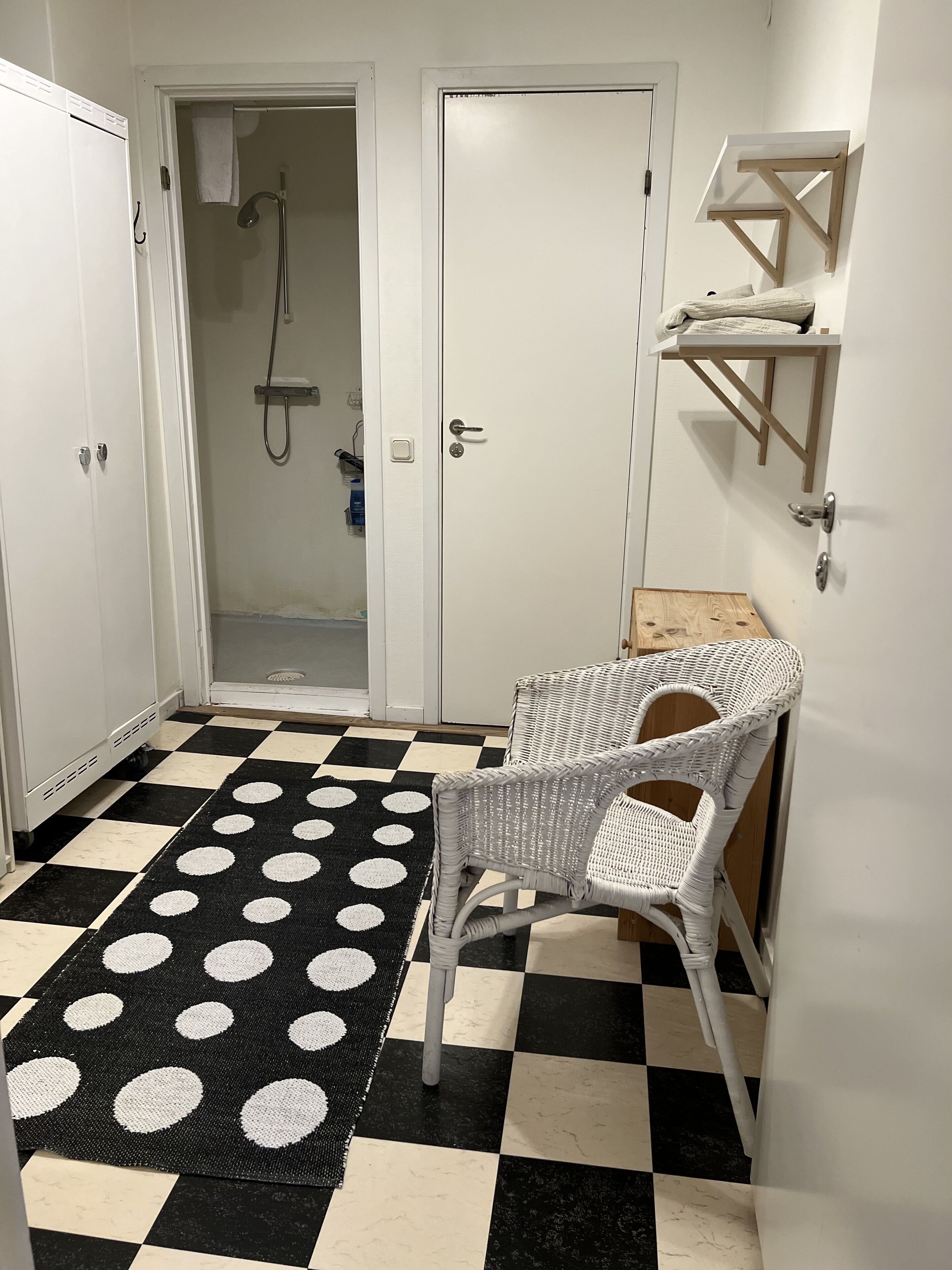 A bathroom with a checkered floor, a white chair, and a shower area.