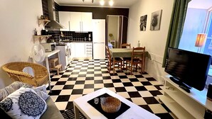 A living room with a checkered floor, a sofa, a coffee table with a magazine, a TV on a stand, and a dining area with a table and chairs. - Hotell Alderholmen (Gävle)