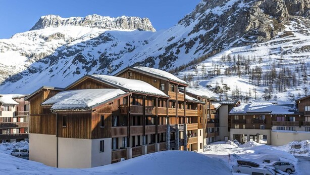 A wooden chalet-style hotel with multiple balconies, set against a backdrop of snow-covered mountains and clear blue sky. - 200m from resort center, balcony, tv, ski locker, 26-30m², Val d'Isère (Val-d'Isère)