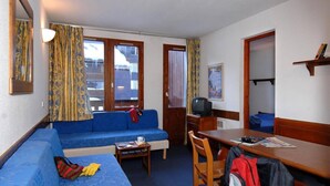 A compact hotel room with a blue sofa, a small table, a TV, and a bed. - 200m from resort center, balcony, tv, ski locker, 26-30m², Val d'Isère (Val-d'Isère)
