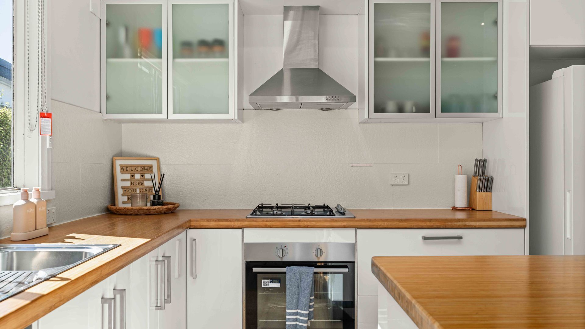 A modern kitchen with white cabinetry, a stainless steel range hood, and a built-in oven.