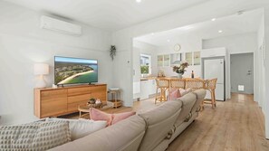 Un salon moderne doté d’un téléviseur à écran plat, d’un meuble en bois, d’un canapé beige et d’un coin repas avec une table et des chaises.