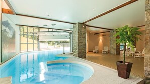 Une piscine intérieure avec un jacuzzi, des murs en pierre et une vue sur l’extérieur.