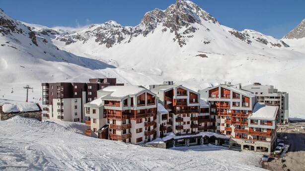 Et skisportssted med sneklædte bjerge og høje bygninger med altaner og langrend.