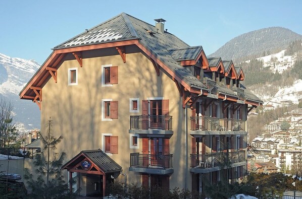 A multi-story building with balconies and a ski lodge sign, surrounded by mountains and snow.
