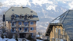 A multi-story building with a sloped roof, balconies, and a view of snow-covered mountains.