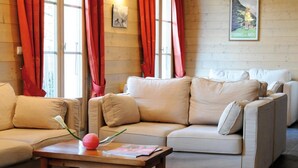 Una sala de estar acogedora con un sofá color beige, una mesa de centro de madera y cortinas rojas.