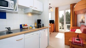A modern kitchen with white cabinets, a microwave, and a coffee maker. There is a dining area with a wooden table and chairs, and a red sofa. - Wifi, swimming pool, terrace, balcony, parking, tv, ski locker, 22m², Font Romeu (Font-Romeu-Odeillo-Via)
