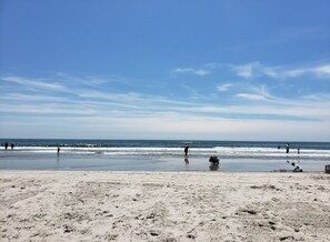A beach with people walking and playing in the sand, and the ocean in the background.