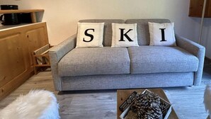 A cozy living room with a grey sofa, three pillows spelling out "SKI," a wooden cabinet, and a small table with pinecones and a remote control. - 150m from ski slopes, 2nd floor, tv, 37m², Méribel (Méribel - Les Allues)