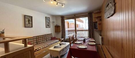 A cozy living room with a sofa, a dining table set for two, and a wooden bench.