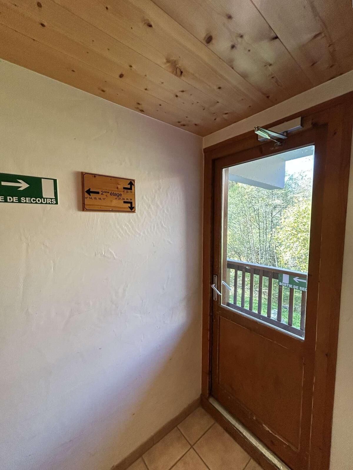 A hallway with a wooden ceiling, a door with a window, and a green exit sign.