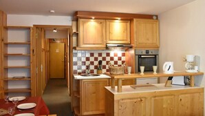 A compact kitchen with wooden cabinets, a tiled backsplash, and a dining area with a table set for four. - 150m from ski slopes, 2nd floor, tv, 37m², Méribel (Méribel - Les Allues)