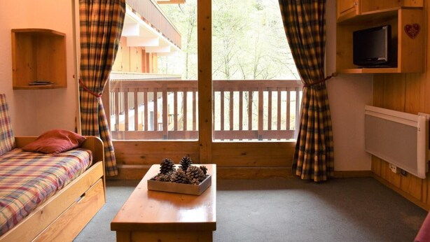 A cozy cabin room with a bed, a small table with pinecones, a TV, and a balcony with a wooden railing. - 150m from ski slopes, 2nd floor, tv, 37m², Méribel (Méribel - Les Allues)